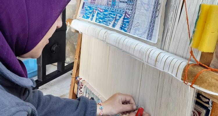 Person, die einen Wandteppich an einem Webstuhl webt.
