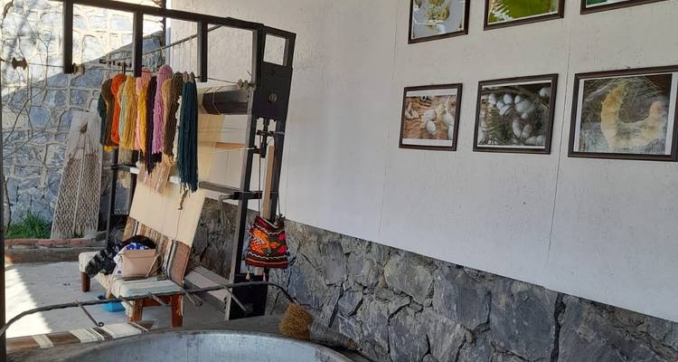 Werkstattinnenraum mit Webmaterialien und gerahmten Bildern.