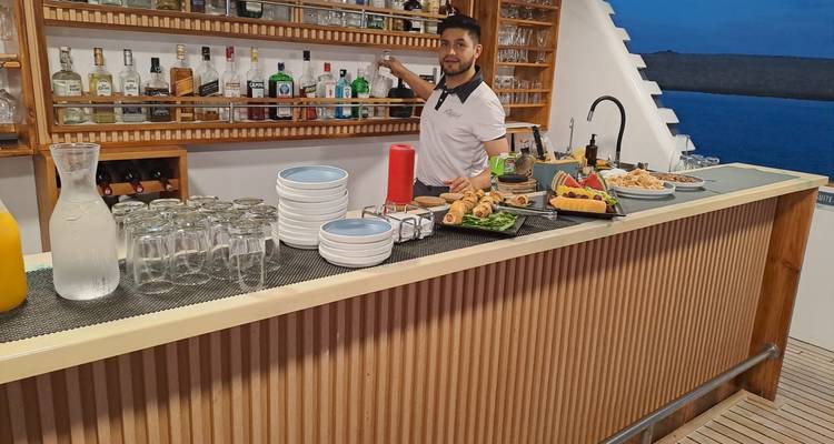 Bartender preparing drinks at an open-air yacht bar stocked with bottles and snacks