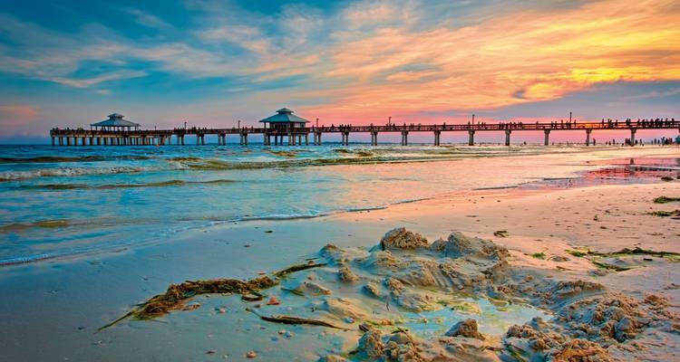 Beach at sunset with a long pier and colorful sky.