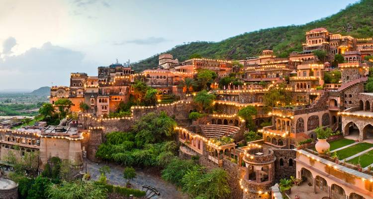 Beleuchtete Terrassen des Neemrana Fort-Palace, die bei Einbruch der Dämmerung einen grünen Hang hinabfallen