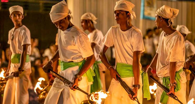 Hombres jóvenes vestidos de blanco con bandas verdes llevan antorchas encendidas durante una procesión cultural nocturna.