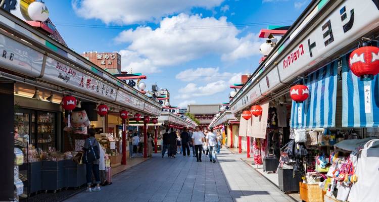 Bustling Nakamise shopping street lined with stalls and red lanterns beneath a blue sky.