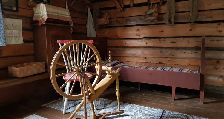 Rustikaler Raum mit einem Spinnrad und einem Holzbett.