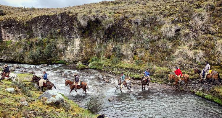 Gruppe von Menschen zu Pferd, die einen Bach in einem bergigen Gebiet durchqueren.