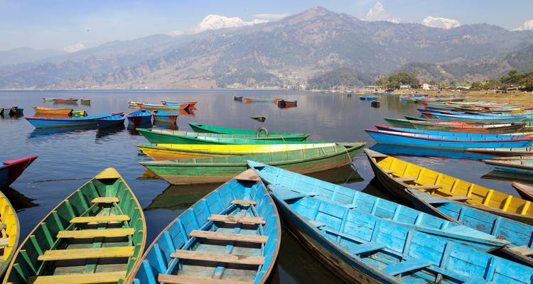 Kleurrijke boten op een kalm meer met bergzicht op de achtergrond.