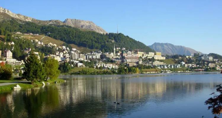 Sparkling lake reflecting the resort town and surrounding forested mountains of St. Moritz.