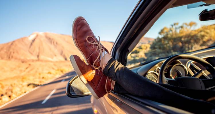 Lässige Sicht auf Füße, die aus einem Autofenster ragen, mit einer Wüstenlandschaft im Hintergrund.