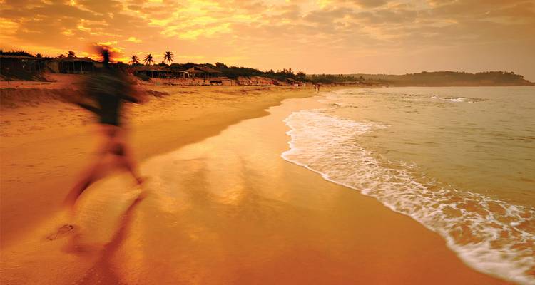 Una figura borrosa trota por una playa al atardecer brillante, las olas lavando la arena.