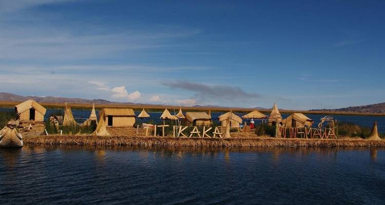Reed island settlement with thatched huts and a large ‘Titikaka’ sign floats quietly on calm lake waters.