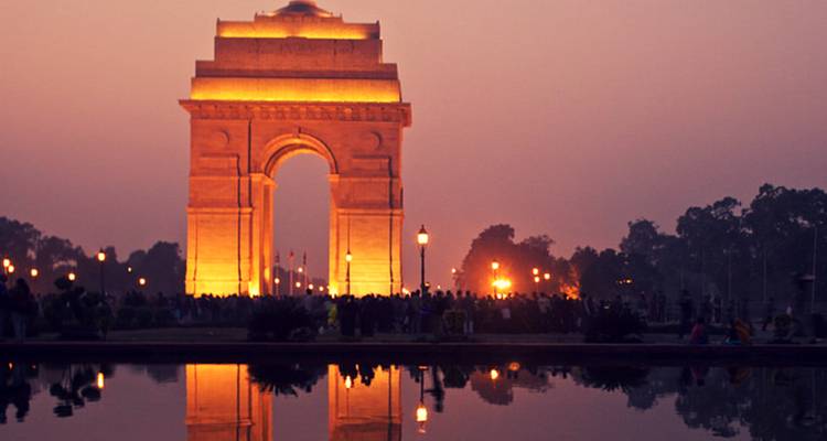 India Gate illuminated at dusk with reflection in water.