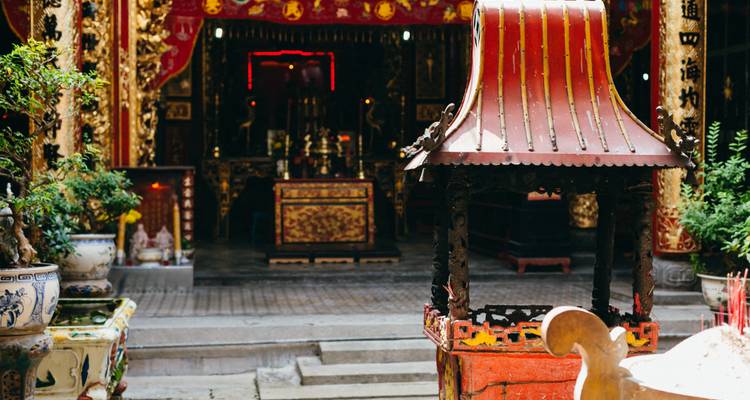 Richly decorated altar and red incense burner inside an ornate Vietnamese temple.