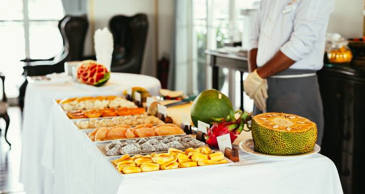 Elegant buffet table on a river cruise displaying tropical fruit and pastries with staff member nearby.