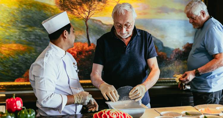 Chef guides guests during an onboard cooking demonstration, preparing rice paper rolls.