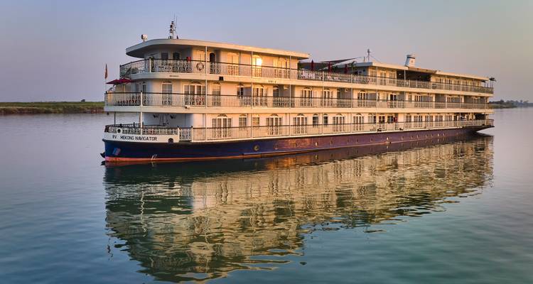 River cruise ship reflecting perfectly on calm water during golden sunrise.