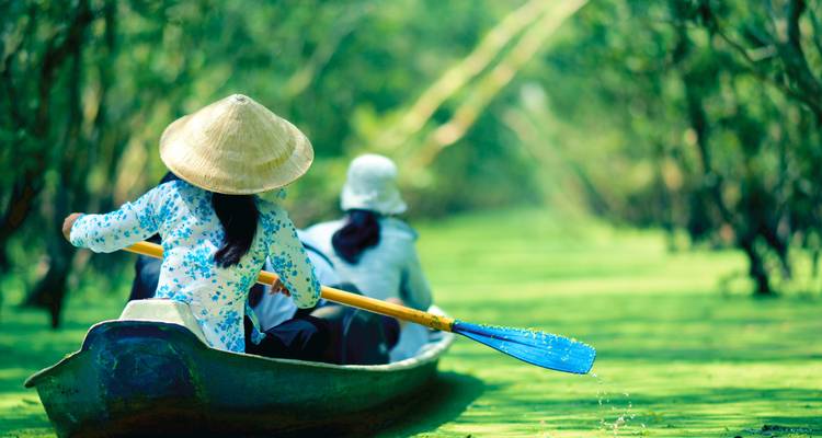 Two people rowing a canoe through a lush, green waterway.