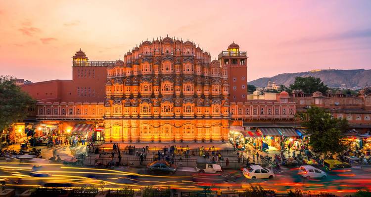 Blick auf das wunderschön beleuchtete Hawa Mahal in der Abenddämmerung mit Verkehr im Vordergrund.