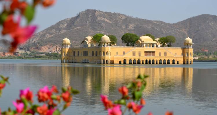 Jal Mahal Palast, gelegen in der Mitte eines Sees mit Blumen im Vordergrund.