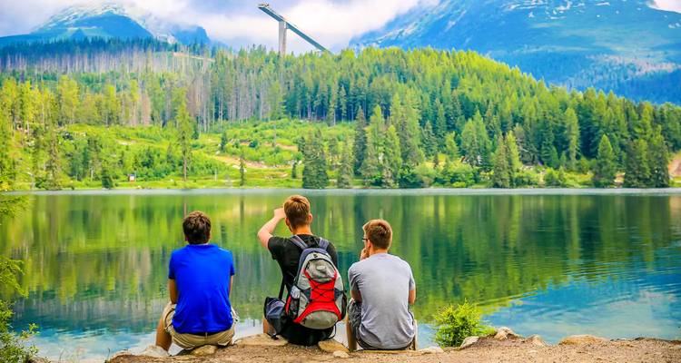 Tres personas sentadas junto a un lago con montañas al fondo.