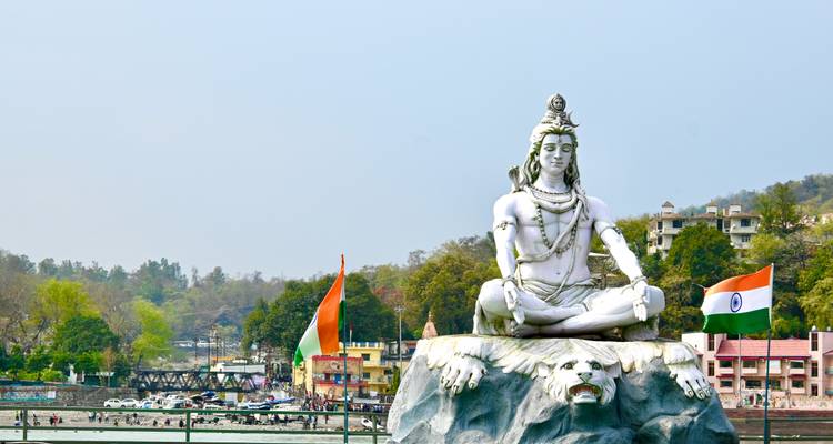 Groot standbeeld van een godheid aan een rivier met vlaggen en groen.