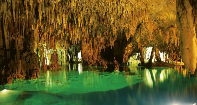 An interior view of a brightly lit underground cave with crystal-clear water.