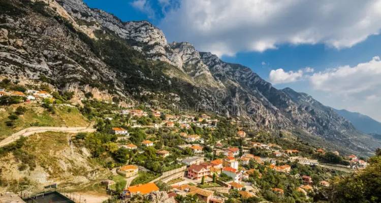 Encantador pueblo en la ladera con casas de tejados rojos anidado bajo empinadas montañas de piedra caliza bajo un cielo brillante.