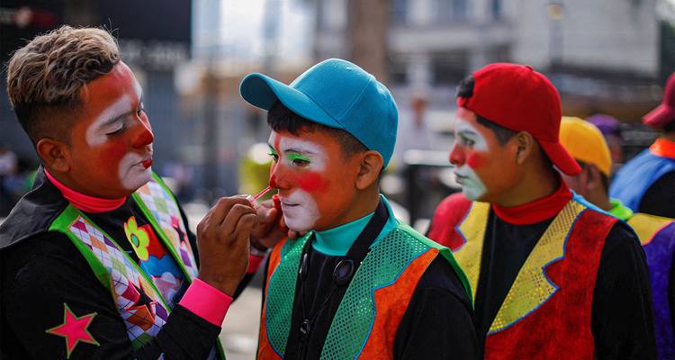 Payasos aplicándose maquillaje facial colorido antes de un desfile callejero.