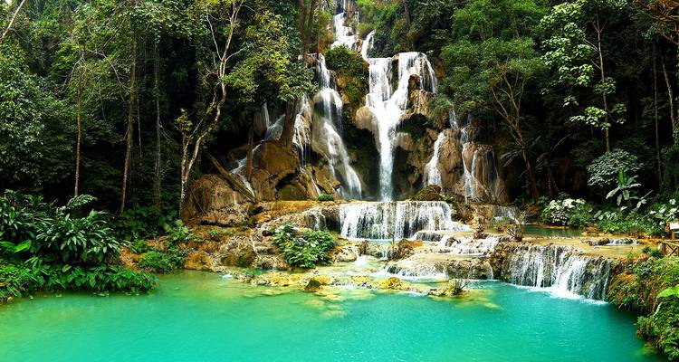 Cascada de Kuang Si con múltiples niveles que cae en piscinas de un turquesa intenso rodeada de bosque verde exuberante.