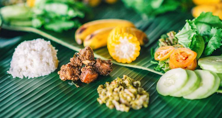 Traditional Filipino meal served on banana leaves with rice, meat, corn and fresh vegetables.