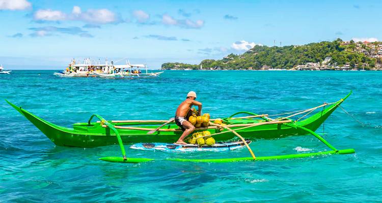 Vendor paddles a bright green banca filled with coconuts across crystal-clear water.