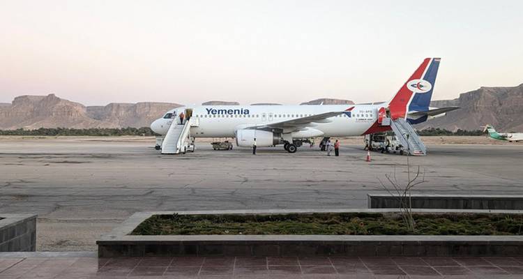Un avión de pasajeros de Yemenia está estacionado en una pista remota del desierto enmarcada por mesas escarpadas mientras los pasajeros abordan por escaleras.