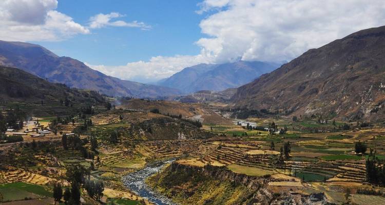 Terraced farmland, winding river and rugged mountains of the Colca Valley under scattered clouds.