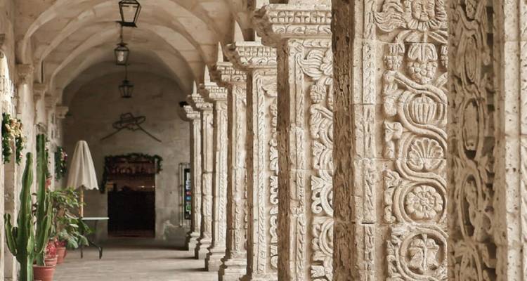 Stone cloister with intricately carved volcanic-rock columns in soft interior light.
