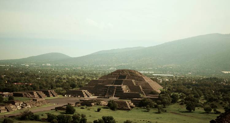 Una amplia vista aérea de la Pirámide del Sol rodeada de llanuras verdes y colinas brumosas a lo lejos.