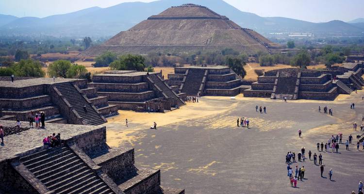 Los visitantes exploran la inmensa plaza y las estructuras de piedra escalonada que conducen a una gran pirámide en Teotihuacán.
