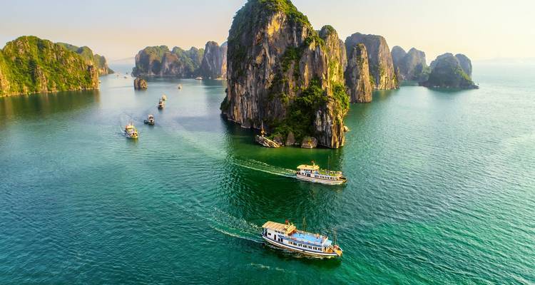 Vue aérienne de bateaux touristiques naviguant dans les eaux vert jade parmi des îles calcaires abruptes.