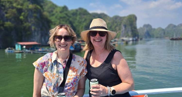 Deux amis savourant des boissons sur un bateau avec des pics calcaires et une eau verte en arrière-plan.