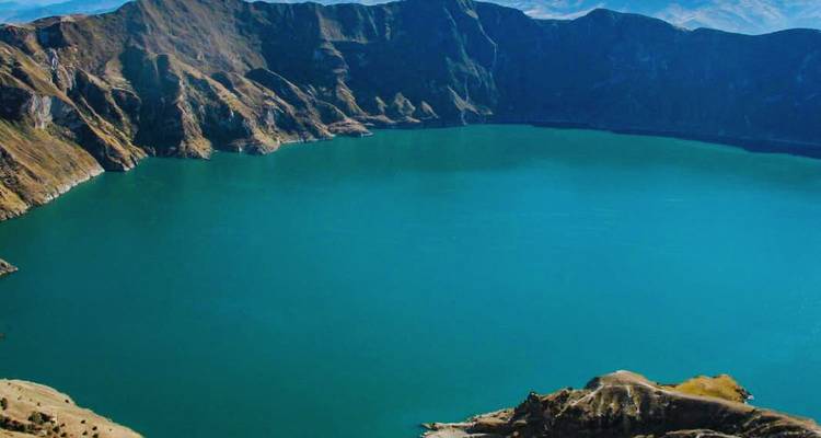 Turquoise crater lake surrounded by steep volcanic walls viewed from above