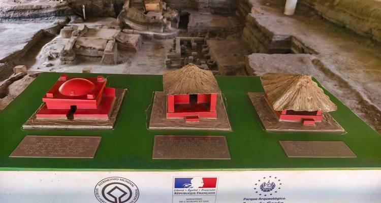 Scale models of ancient structures displayed inside an archaeological museum above excavation pits
