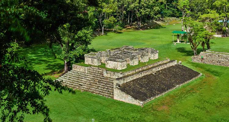 Small stone pyramid and terraces in a lush green archaeological park