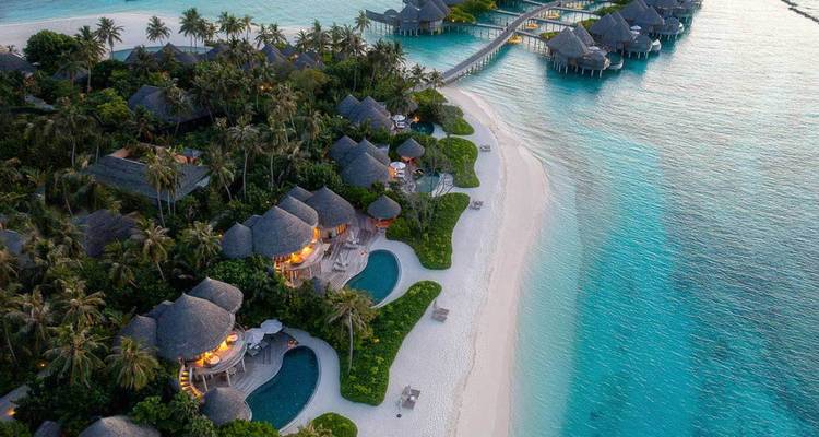 Aerial view of a lush island resort with pools, white sand beach and turquoise lagoon.