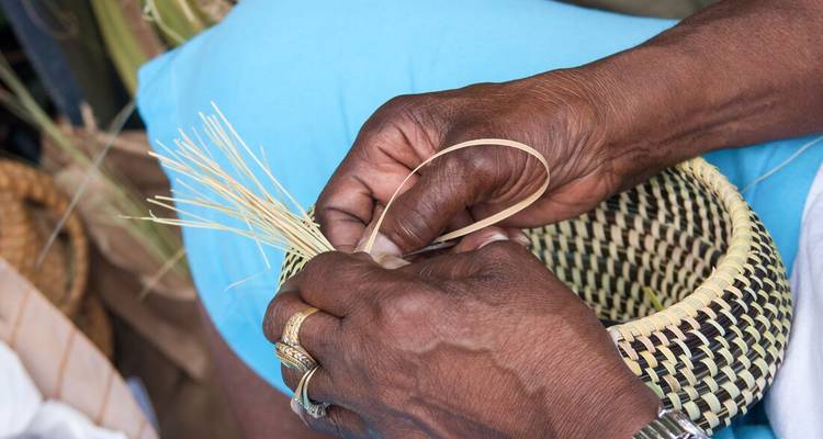 Close-up of skilled hands weaving a traditional sweetgrass basket.