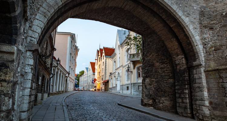 Cobblestone lane passes beneath a massive stone arch in the quiet early morning of Tallinn.