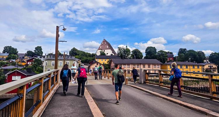 Walkers cross a bridge toward the quaint wooden houses and white-roofed church of Porvoo.