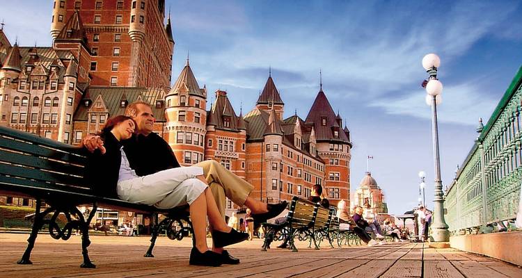 Romantic couple relaxing on a wooden boardwalk bench with Château Frontenac’s turrets rising behind them.