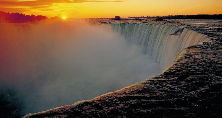 Sunset view over Niagara Falls with mist rising as the sun dips below the horizon.