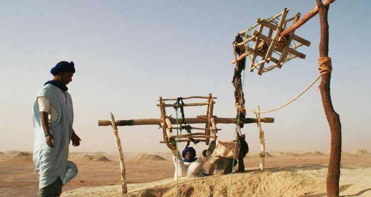 Des hommes locaux exploitant un mécanisme traditionnel de puits du désert contre l'horizon sablonneux