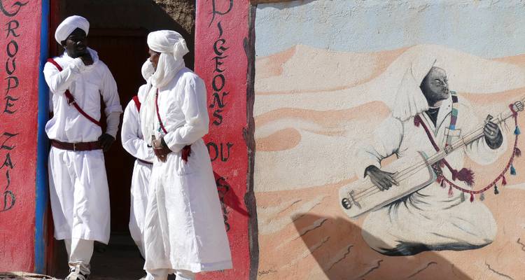 Deux musiciens en robes blanches conversant à côté d'une fresque colorée représentant un instrument traditionnel