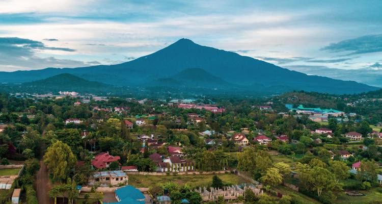 Une vue aérienne d'Arusha s'étend sous la silhouette dramatique du Mont Meru dans un ciel matinal doux.