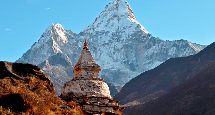 Snow-clad Himalayan peak towering above a Buddhist stupa and rugged valley